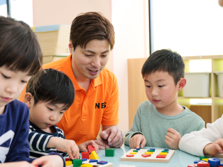 指導者と子どもたちが机で教材を使って学習している様子